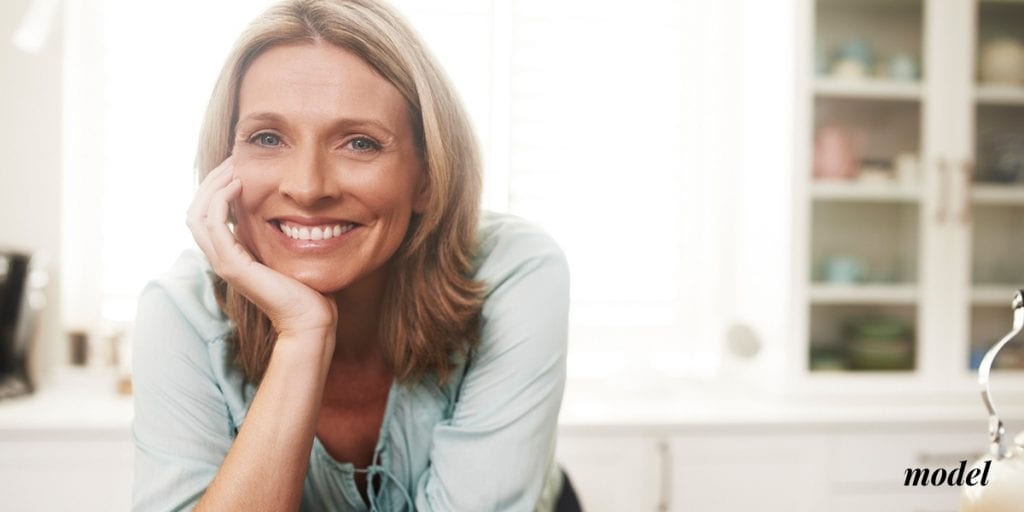 Happy Middle Aged Woman Leaning Over Counter Resting her Chin in her Hand